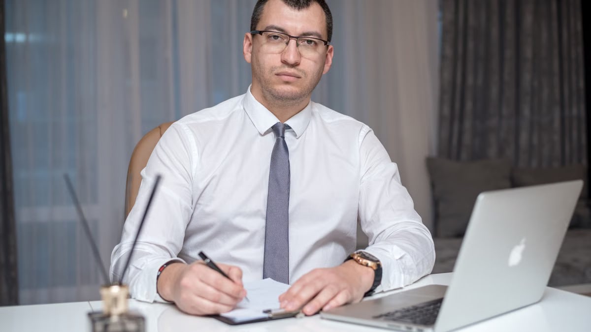 Professional man in corporate attire sitting at desk with laptop, engaged in work.